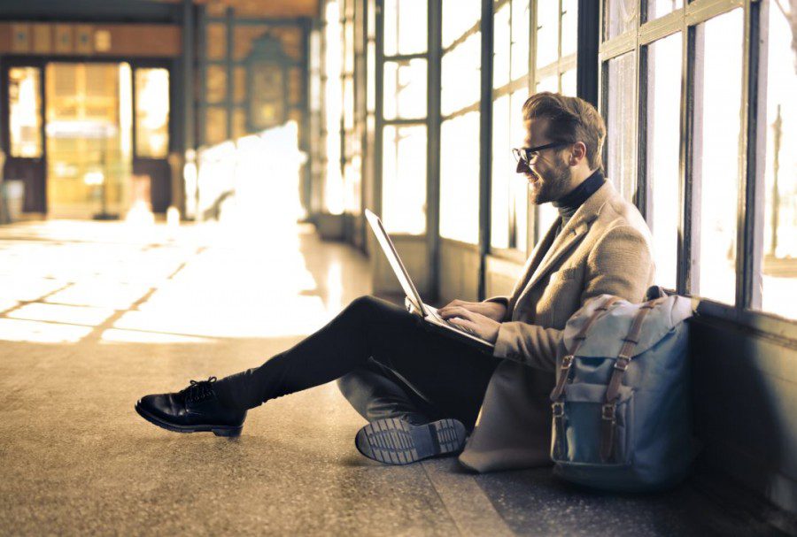 Man sitting near a window looking at his laptop. Learn how to avoid geo-blocking when traveling.